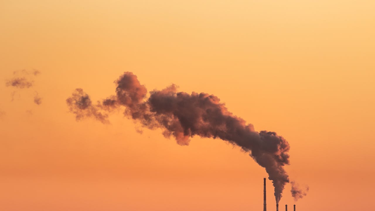 Smoke billowing from industrial chimneys against a vibrant orange sunset sky in Gdańsk, Poland.